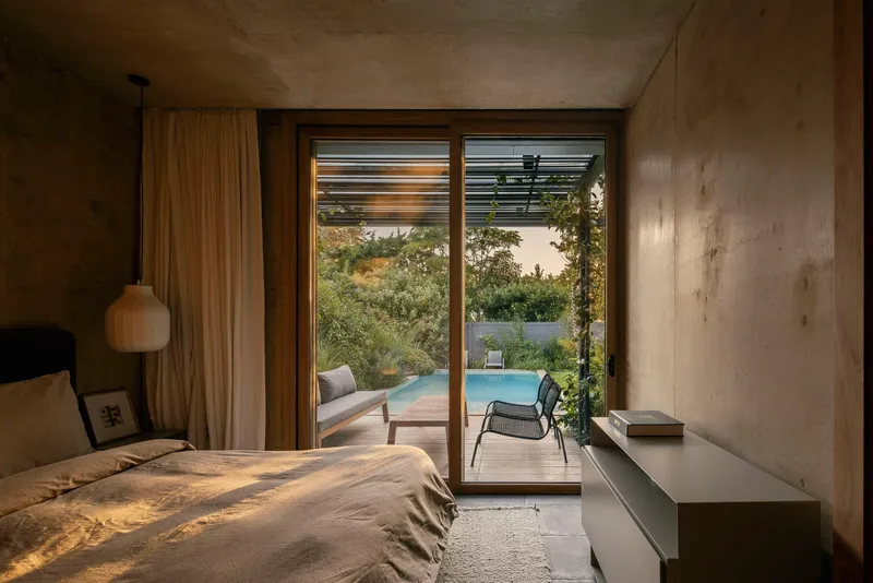 Bedroom with glazed doors opening to terrace with pool and vegetation in evening light