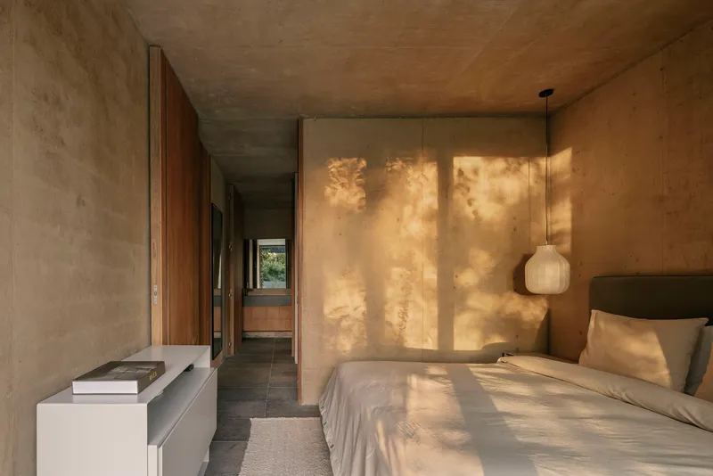 Bedroom corridor with dappled sunlight filtering through exterior louvers onto textured plaster wall