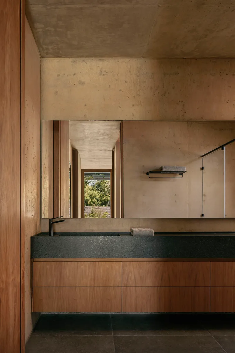 Bathroom vanity with timber cabinetry and black stone sink beneath exposed concrete ceiling