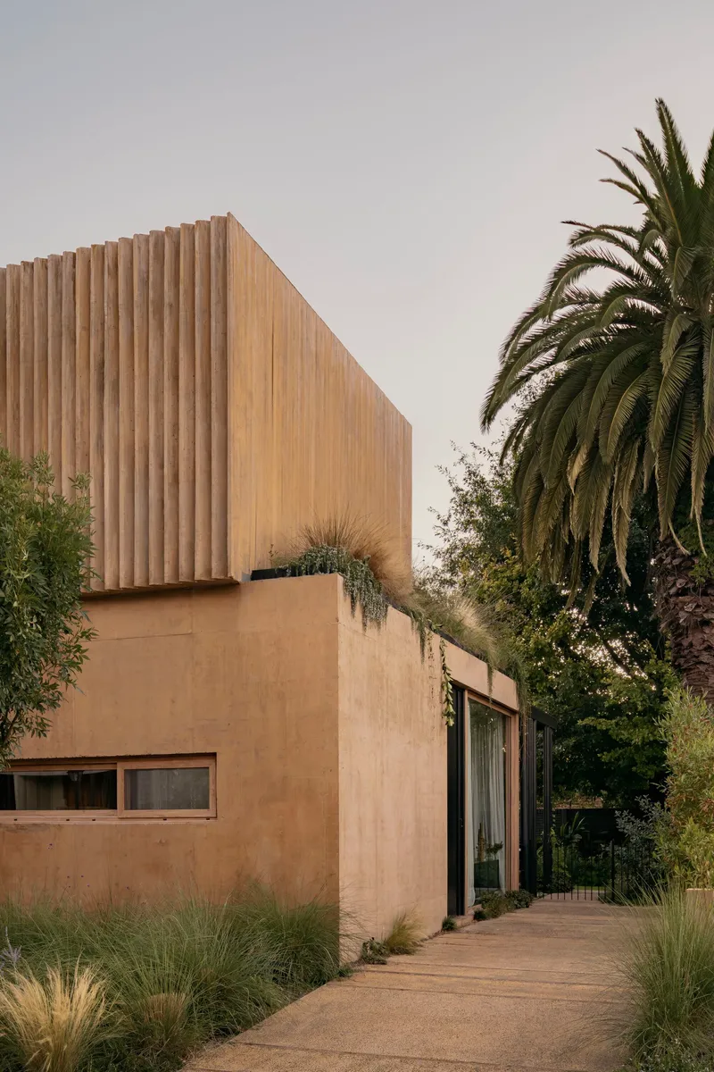 Exterior facade with vertical timber screens above rendered concrete base flanked by palm and olive trees