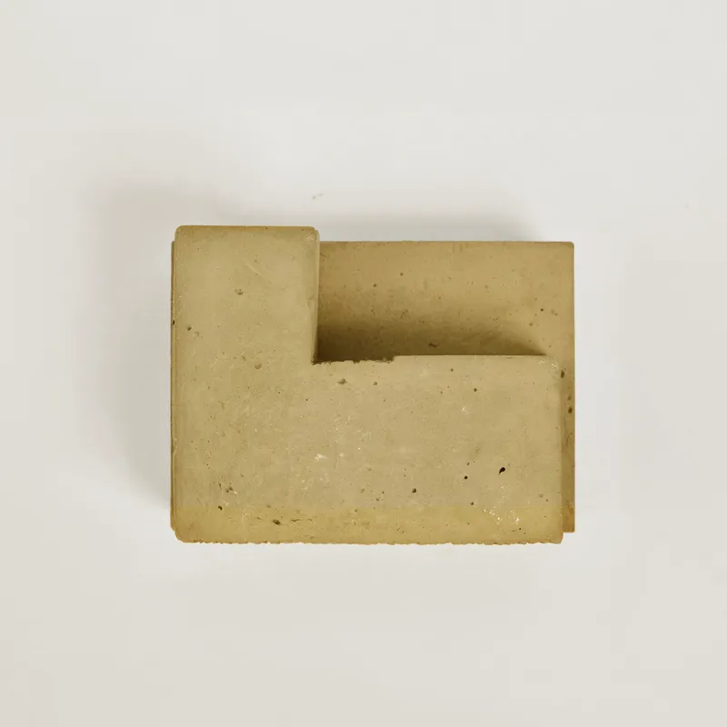 Top-down view of a cast concrete block with a recessed geometric notch on a white surface