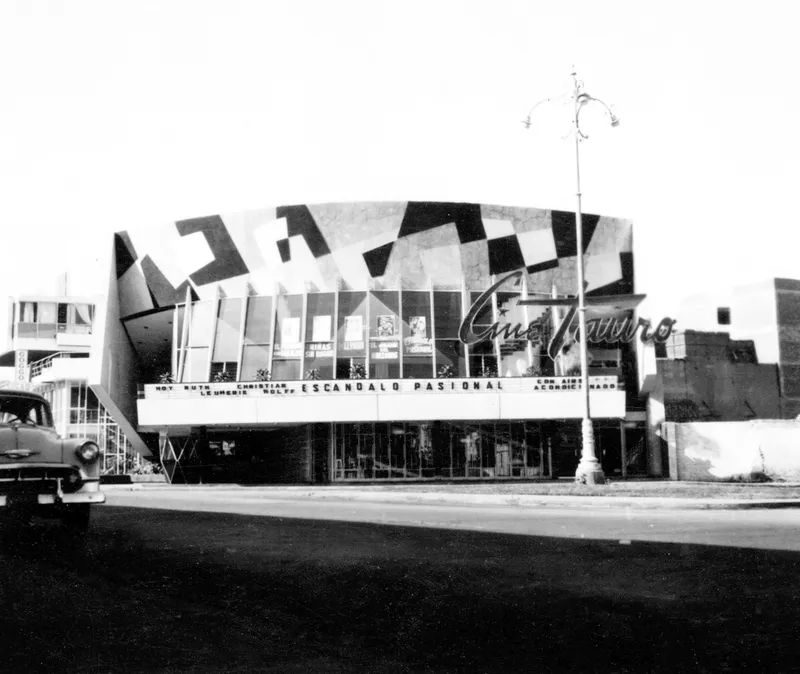 Street view of the cinema facade with geometric roofline and marquee lit by a streetlamp at dusk
