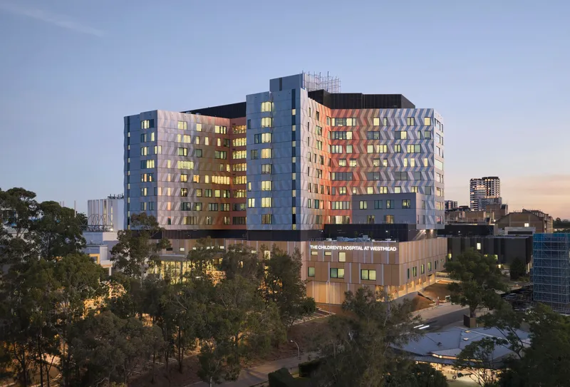 Multi-story hospital building with triangular pattern facade framed by eucalyptus trees at dusk