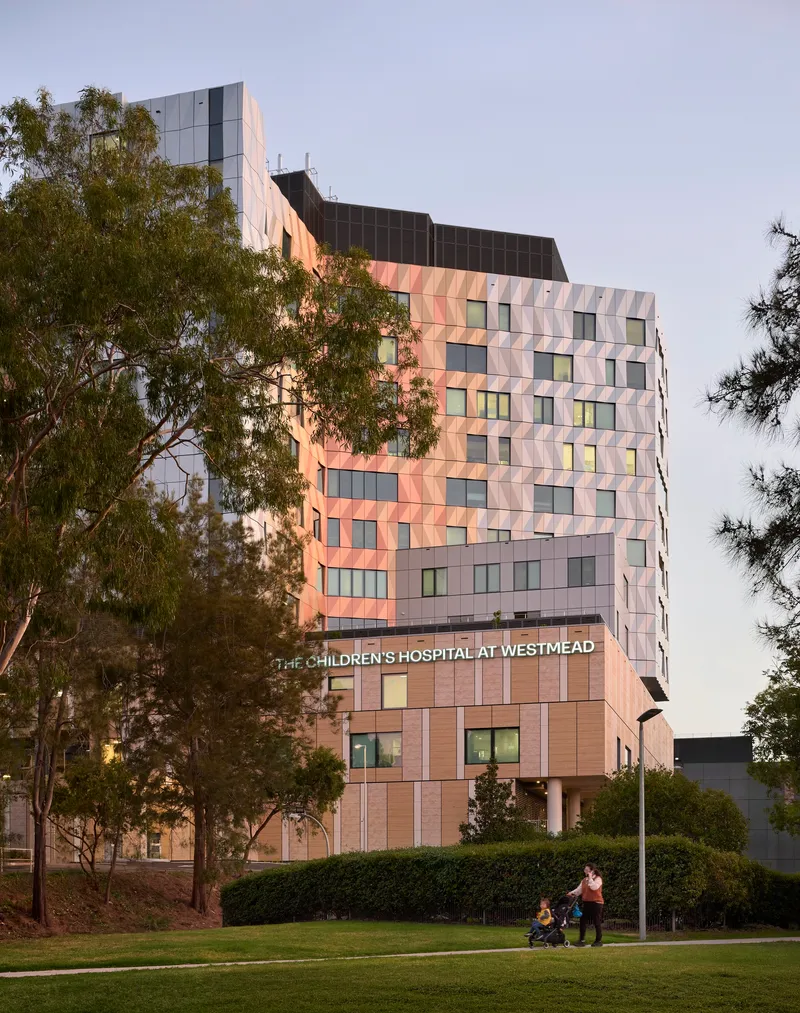 Tower facade with triangular panel cladding in warm and cool tones beside a lawn at twilight