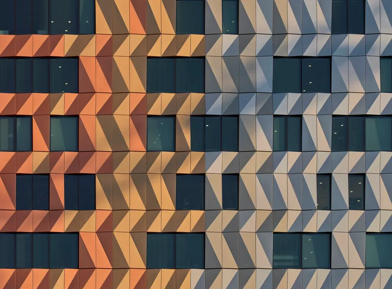 Facade detail of triangular metal panels creating a chevron pattern between horizontal window bands