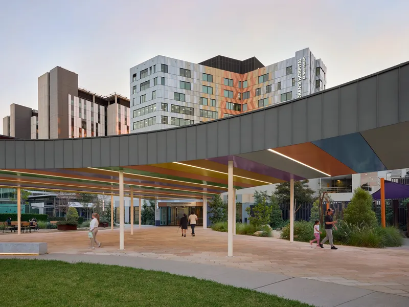 Outdoor courtyard with canopy structure supported by white columns and families walking through planted beds