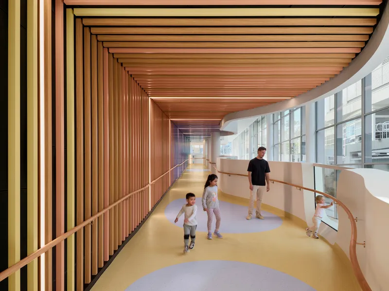 Curved corridor with timber slatted ceiling and yellow flooring as children walk beside glazed wall