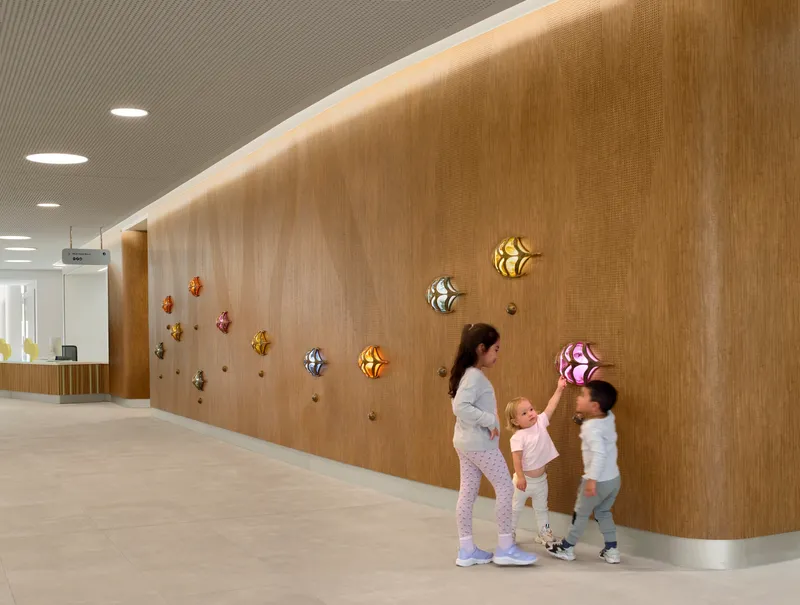 Curved timber wall with colorful wall-mounted lights and a woman with two children reaching toward them