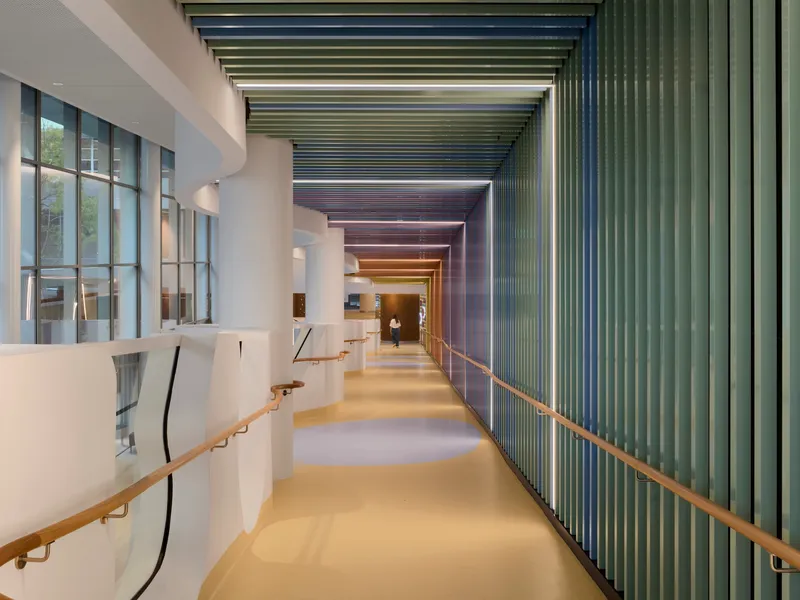 Corridor with colorful vertical metal fins on the wall and timber handrails under slatted ceiling