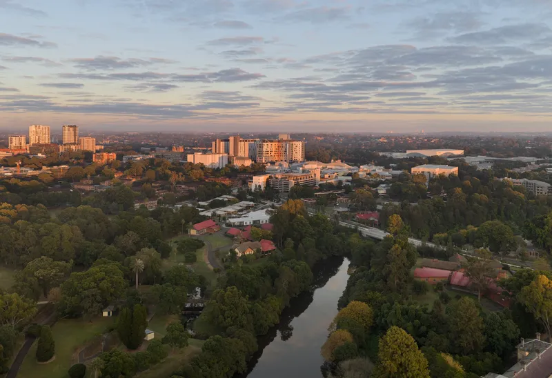 Aerial view of campus surrounded by autumn treetops and winding waterway under dawn sky