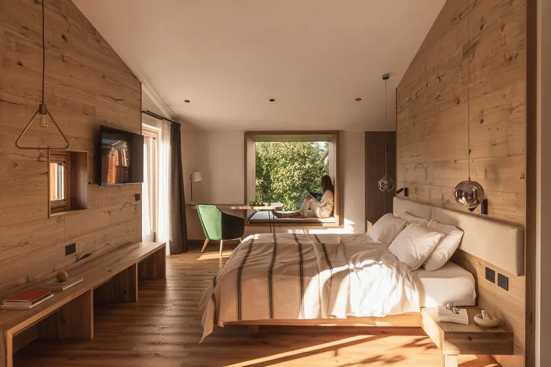 Bedroom with horizontal timber plank walls and wide framed window opening to garden in morning light