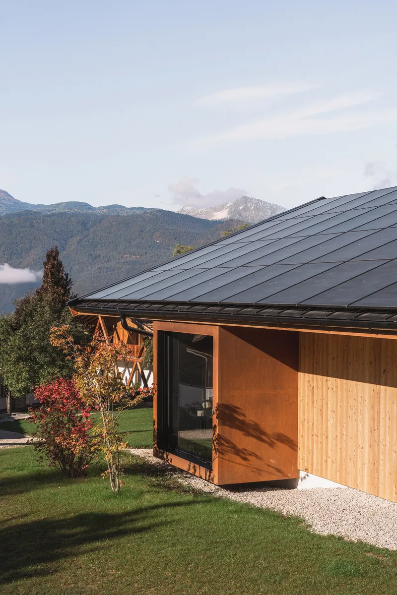 Cantilevered weathered steel volume with timber cladding beneath a dark metal roof at dusk