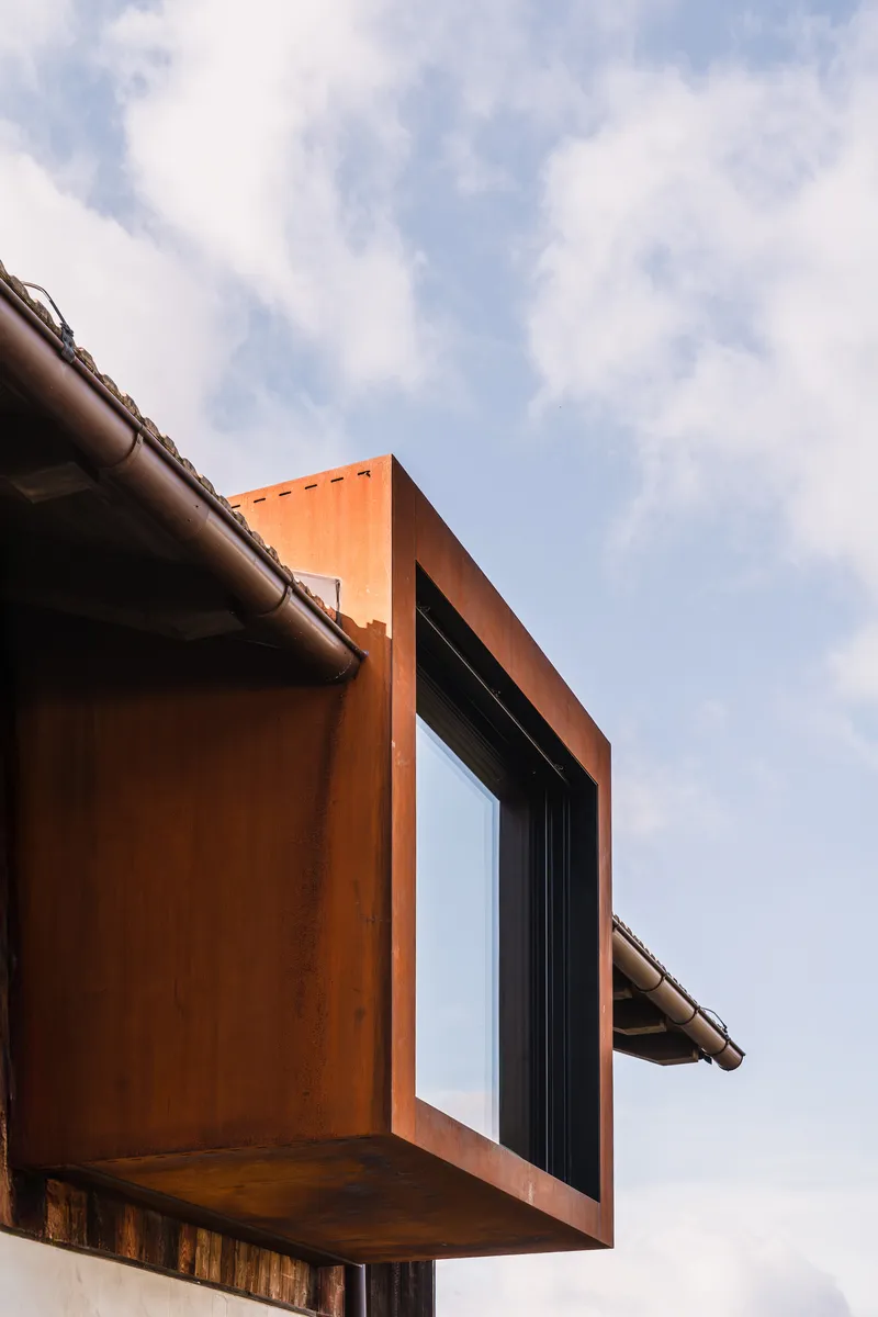 Cantilevered weathered steel bay window framed against a cloudy sky