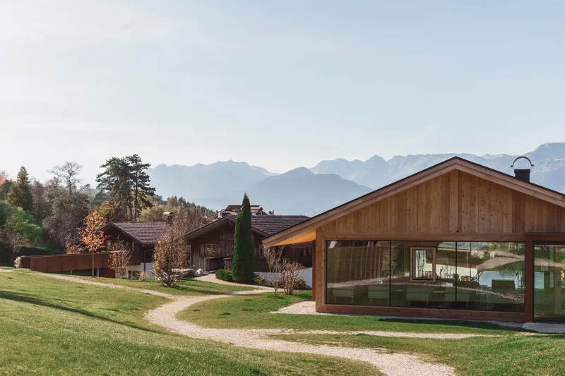 Cluster of gabled timber volumes with glazed walls set in a meadow with mountain views