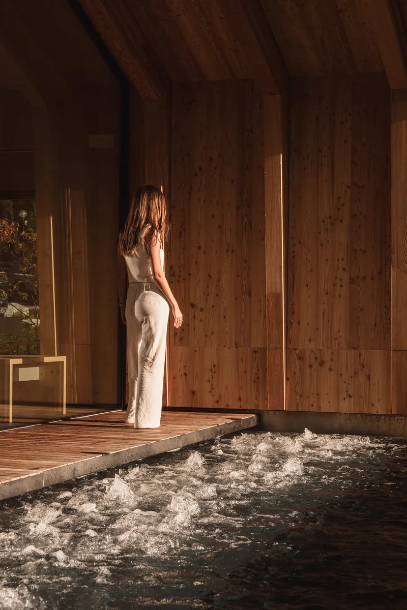 Interior pool edge with vertical light slot in wood wall and figure standing in sunlight
