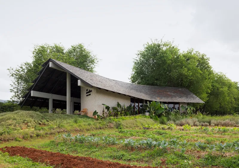 Pitched roof pavilion with brick walls and exposed timber frame amid cultivated vegetable plots