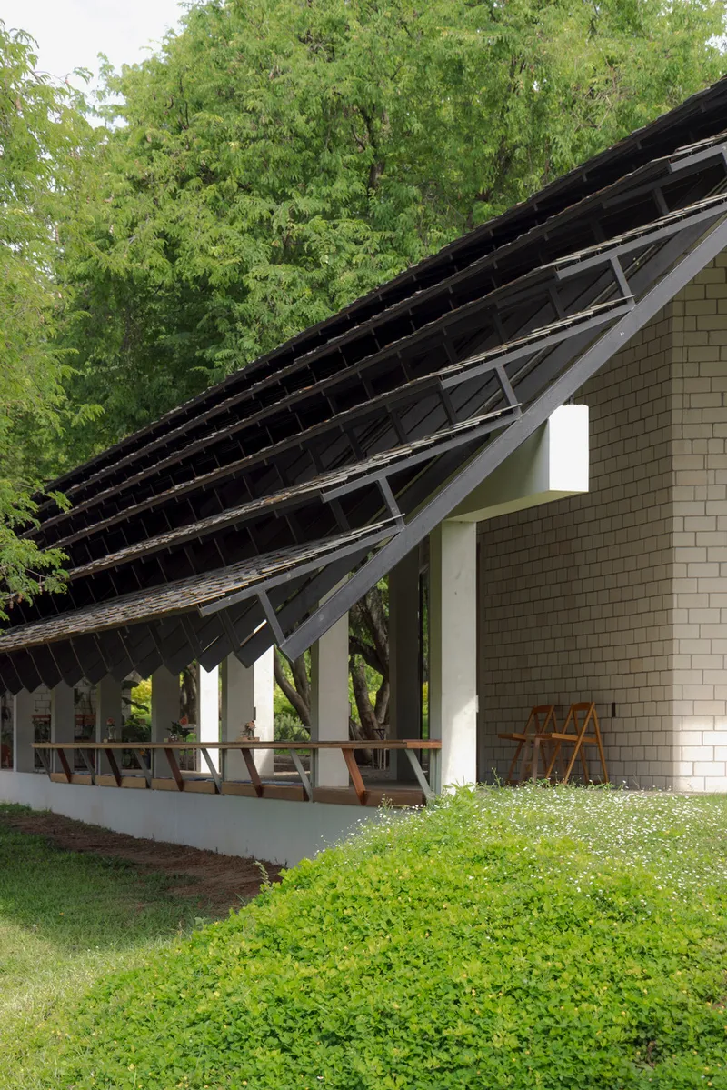 Corner detail of exposed roof structure with timber rafters and white columns beside flowering groundcover