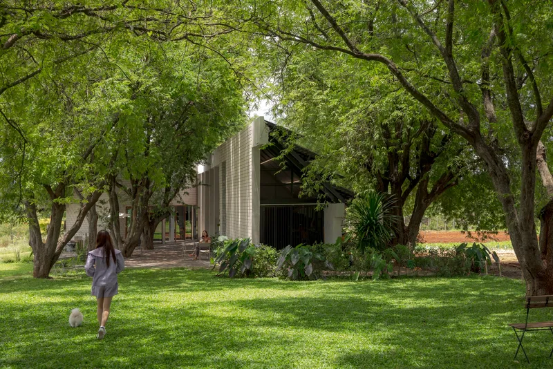 Corrugated metal facade with pitched roof behind a person walking across sunlit grass under trees