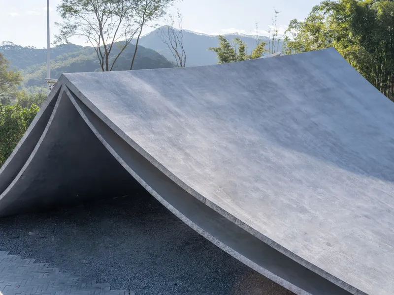 Angular concrete roof with folded planes set against forested mountains under daylight