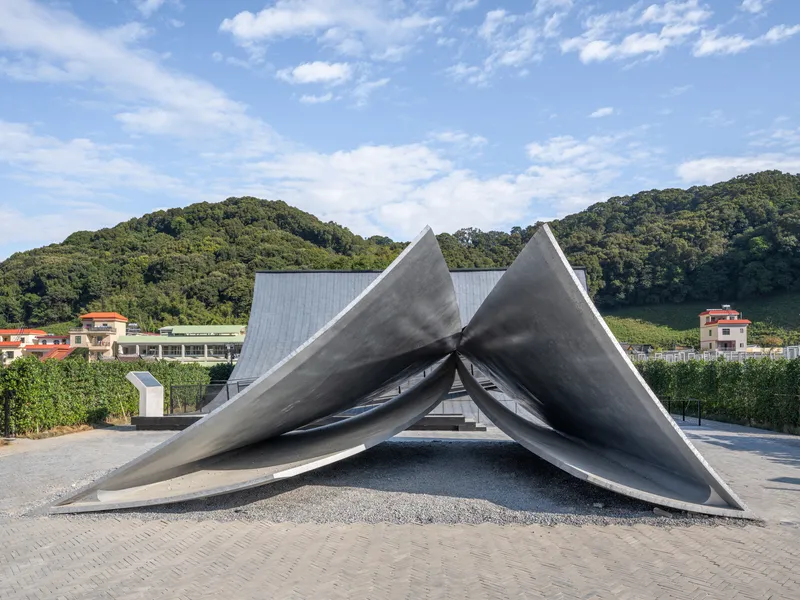 Three intersecting peaked concrete planes forming a shelter against forested hills