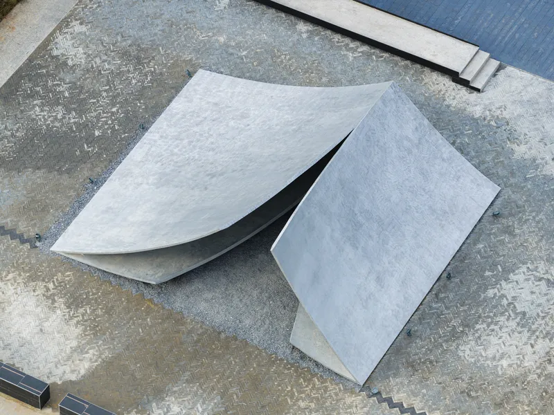 Overhead view of folded concrete planes meeting at sharp angles on a patterned paving