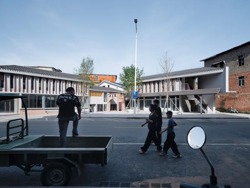 Street view of two symmetrical buildings with vertical louvered facades and people walking across the foreground