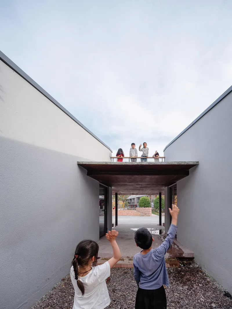 Courtyard view through a timber-roofed passageway with people standing on the rooftop terrace above