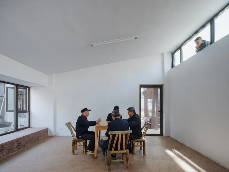 Double-height interior space with people seated at a timber table and a figure visible at the upper window