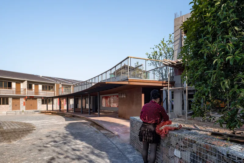 Pavilion with rust-colored metal cladding and rooftop terrace as a resident tends a wire gabion planter at dusk