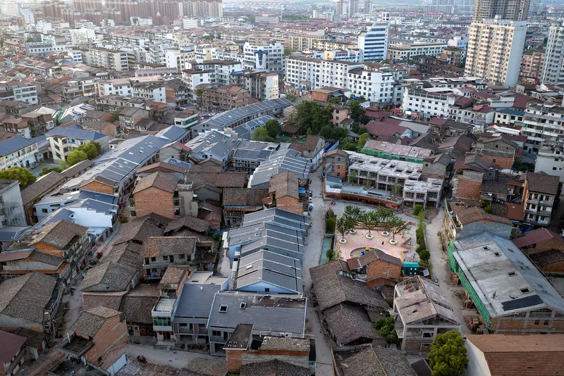 Aerial view of metal-roofed pavilion nestled among low-rise residential blocks in a dense urban neighborhood