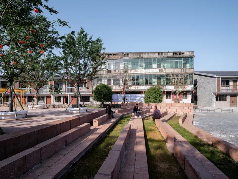 Public plaza with stepped concrete seating and planted strips under a tree canopy in daylight