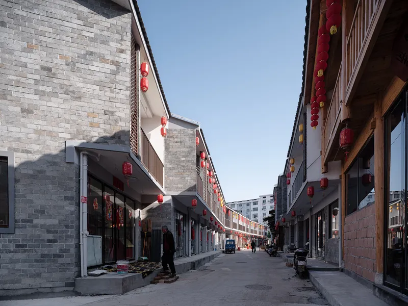 Narrow street lined with grey brick facades and red lanterns strung overhead in twilight