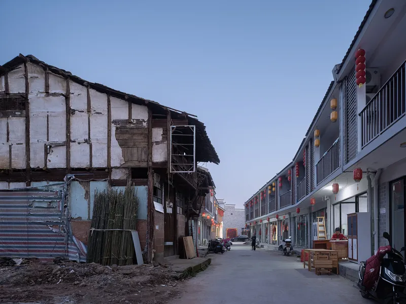 Street view showing a weathered timber building beside a new residential block at dusk