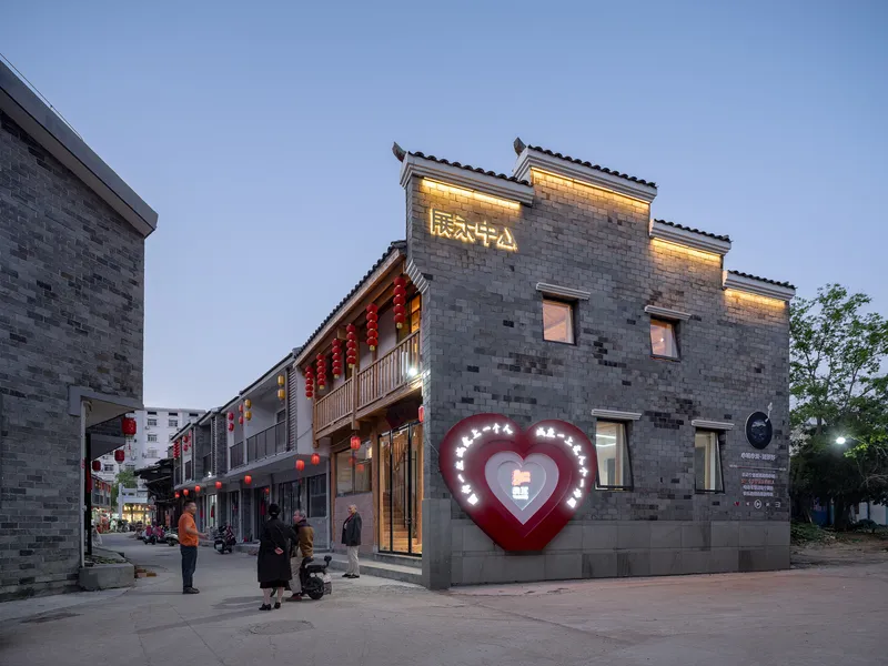 Corner building with grey brick facade and illuminated heart-shaped sign at evening