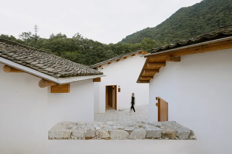 Courtyard with white stucco walls, timber eaves, tile roofs, and a figure walking through