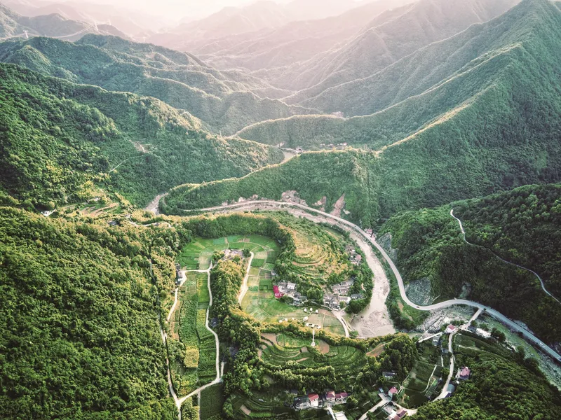 Aerial view of terraced agricultural fields and clustered buildings nestled in a forested mountain valley