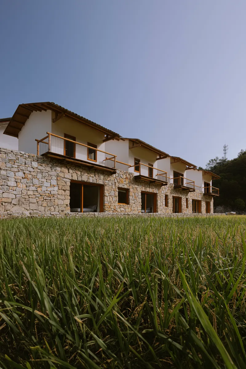 Ground-level view of stone-clad lower walls with timber-railed balconies above a grassy field at twilight