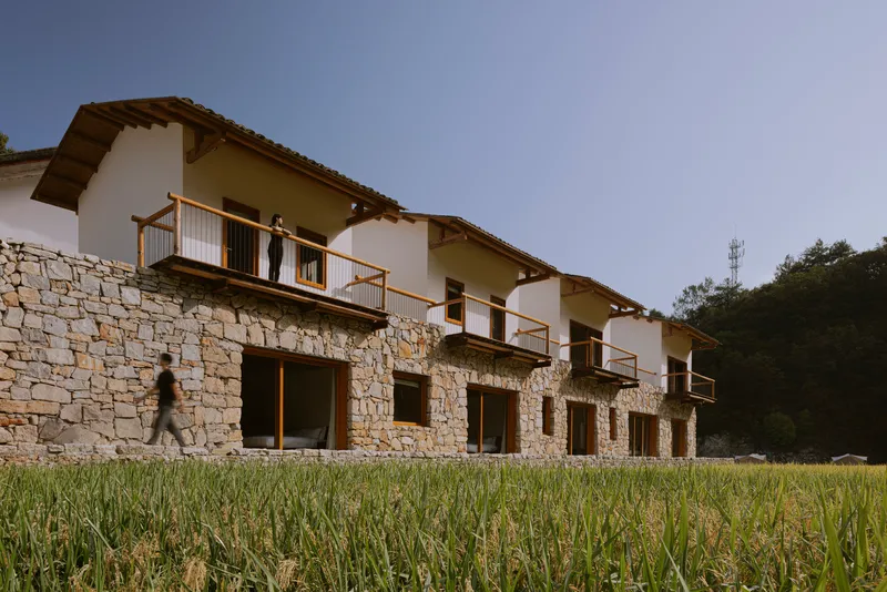 Stone base with upper white volumes and timber balconies with a person standing and another walking