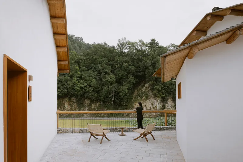 Courtyard terrace with timber loungers facing a pond and wooded hillside under overcast sky