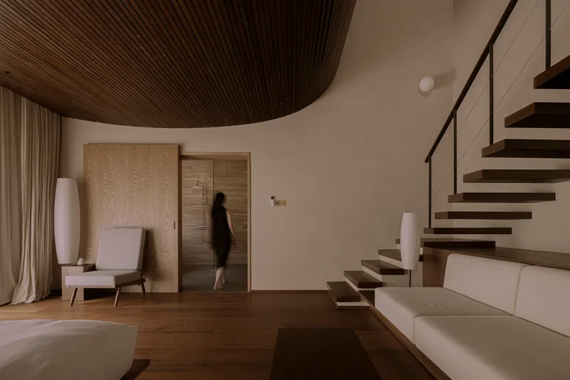 Interior living space with curved timber ceiling and a figure ascending the cantilevered staircase