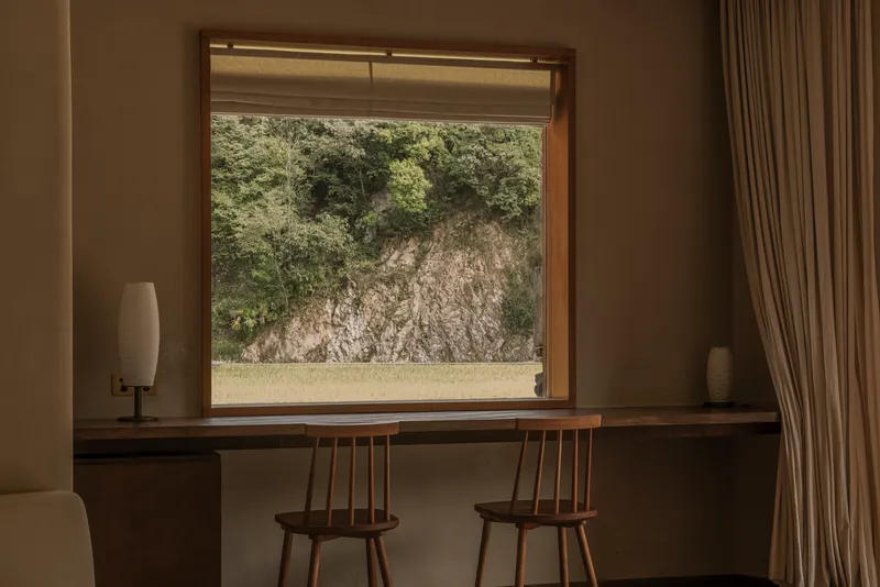 Framed window view of exposed rock outcrop with wooden desk and spindle-back chairs below