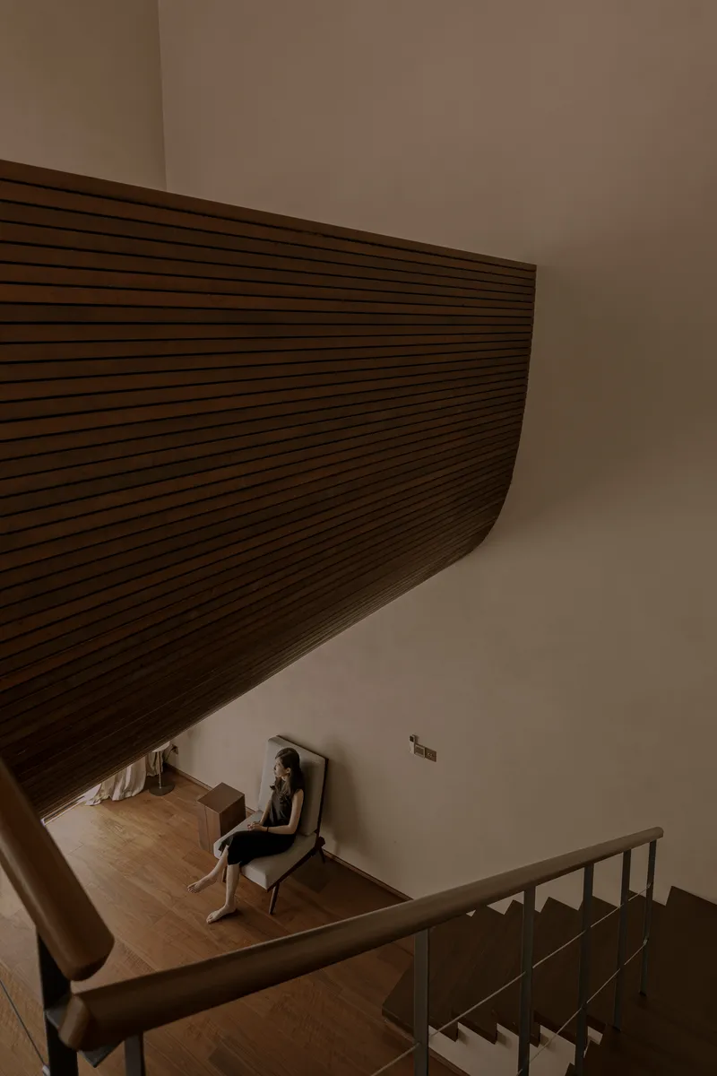 View down stairwell showing curved timber ceiling soffit and a person seated in reading nook