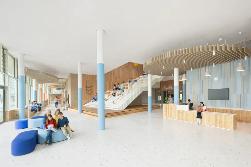 Entry lobby with timber reception desk, slatted ceiling feature, and white columns with blue bases
