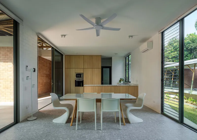 Open plan dining and kitchen space with timber cabinetry and corner glazing overlooking planted garden areas