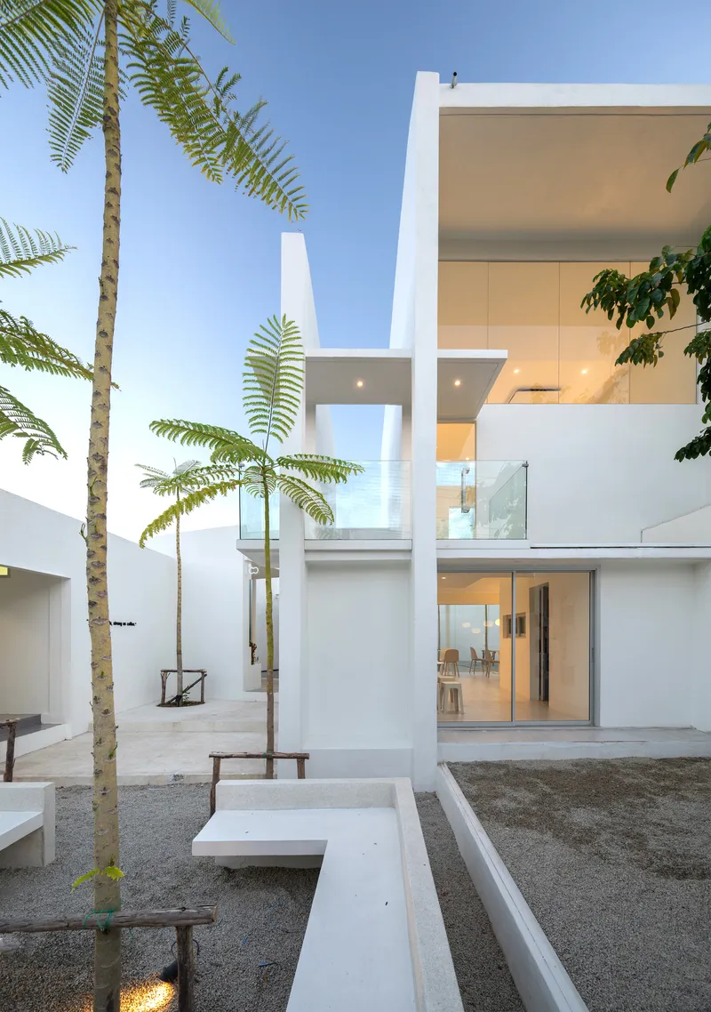 Courtyard view showing the two-story volume with palm trees and concrete benches under blue sky
