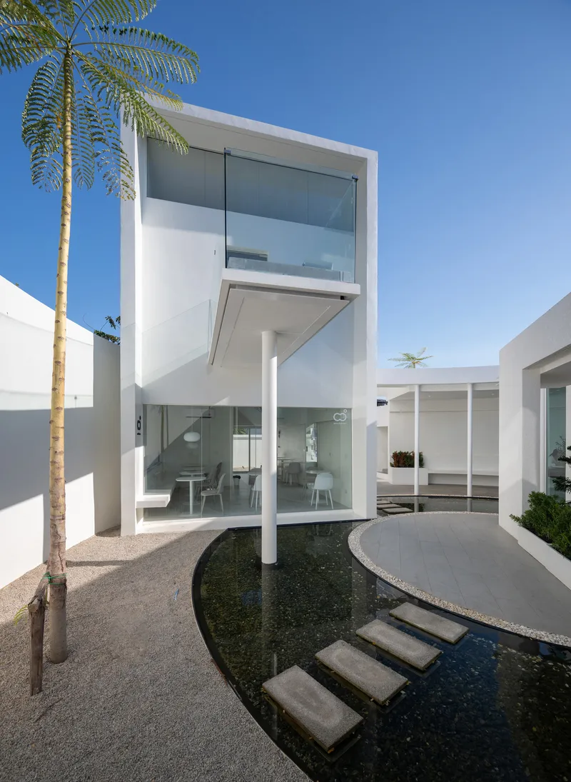 Glass pavilion supported by white columns above a curved reflecting pool with stepping stones