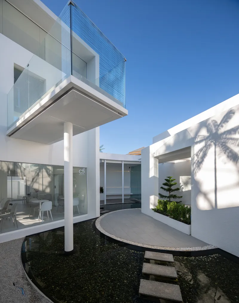 Cantilevered upper floor above a circular water feature with palm shadows on white walls