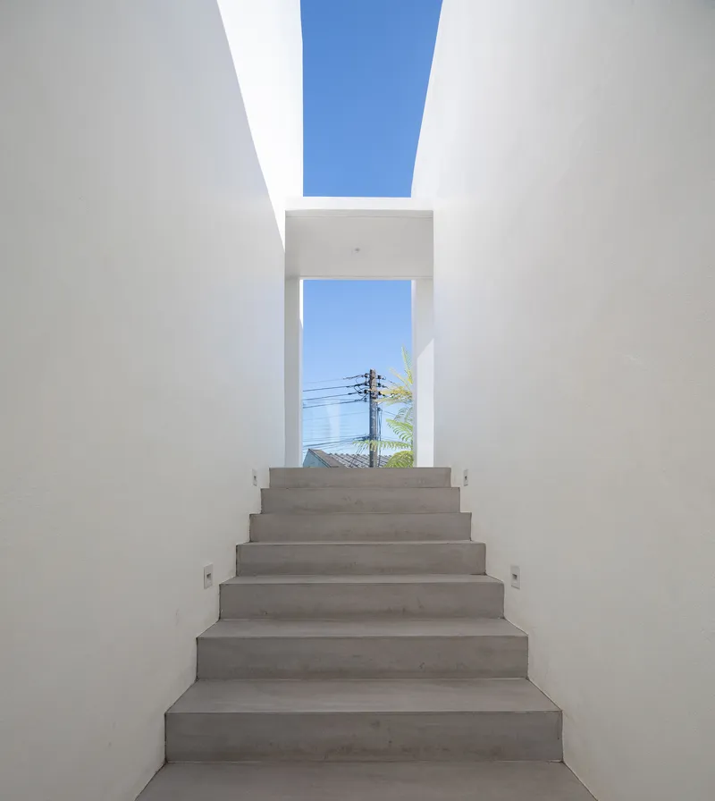 Concrete staircase ascending toward a framed opening and skylight with blue sky beyond
