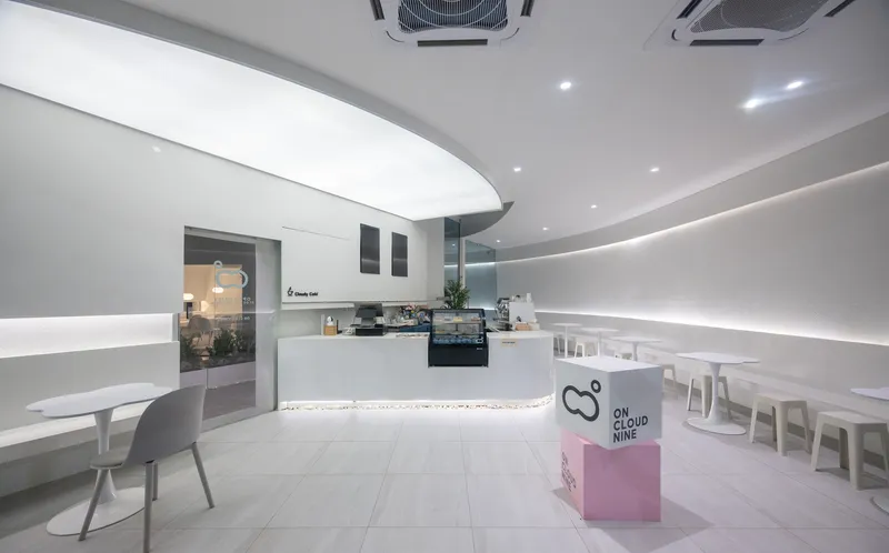 Interior of a cafe with curved counter, continuous LED cove lighting and white seating under recessed ceiling fixtures