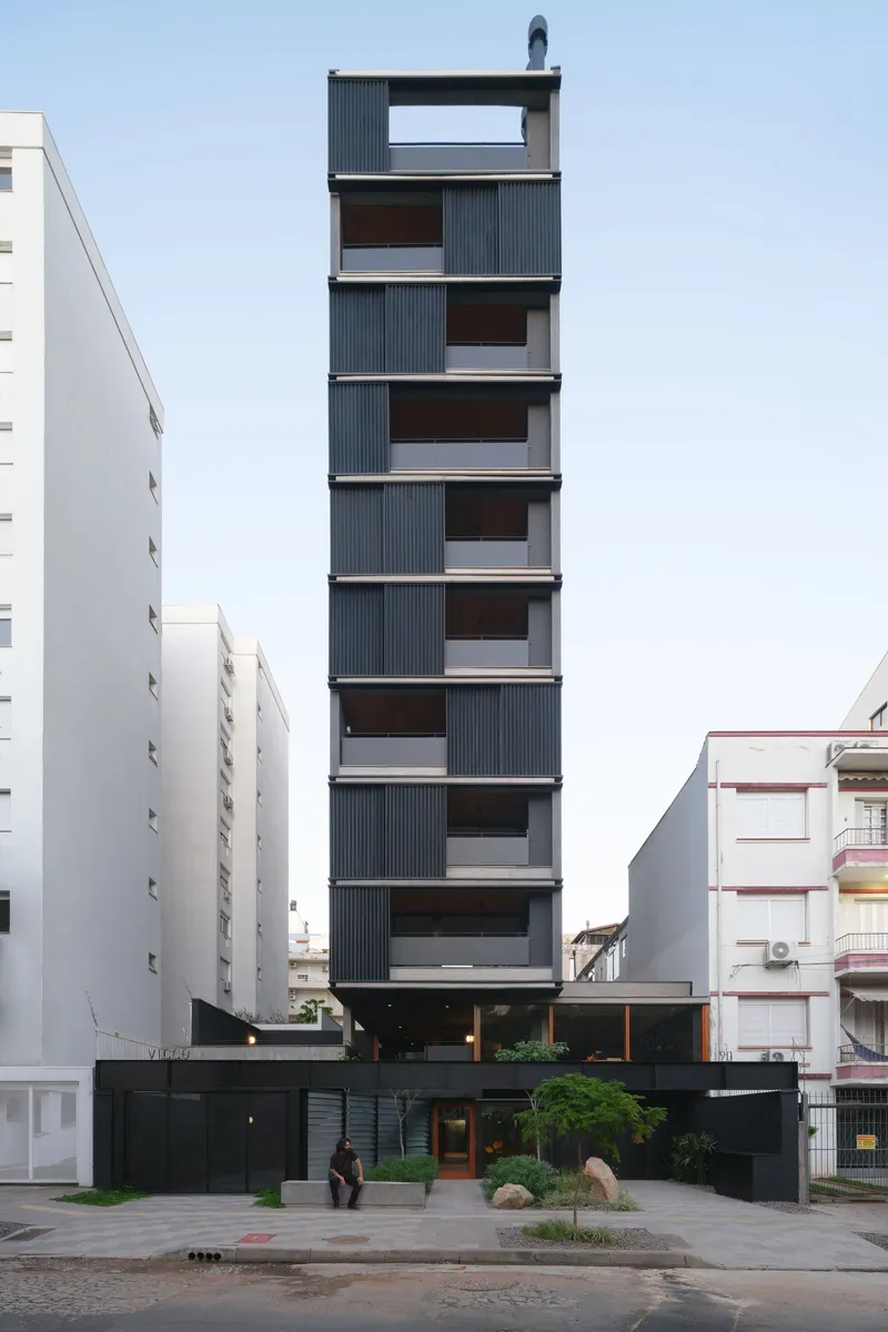 Front elevation of the narrow tower with staggered corrugated metal balconies flanked by white apartment buildings